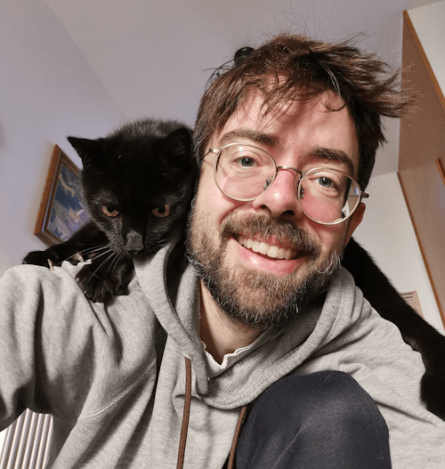 Eine schwarze Katze thront auf der Schulter des Katzensitters. Dieser strahlt über beide Ohren. Beide blicken in die Kamera und sind bereit für weitere Abenteuer :D