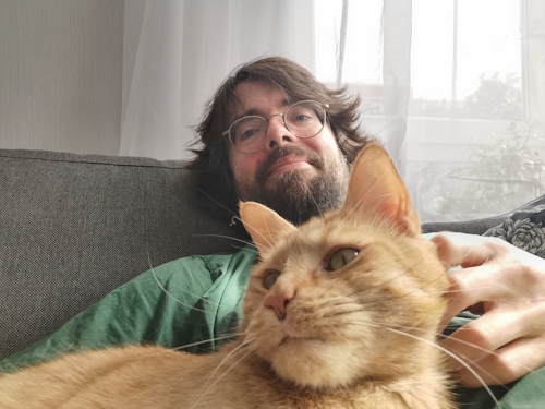 Katzensitter Lukas und Filou sagen: Miau / Hallo & herzlichen Willkommen! Filou, der große Tigerkater, bekommt vom Katzensitter den Hinterkopf gekrault. Beide scheinen mit der Situation hochzufrieden...